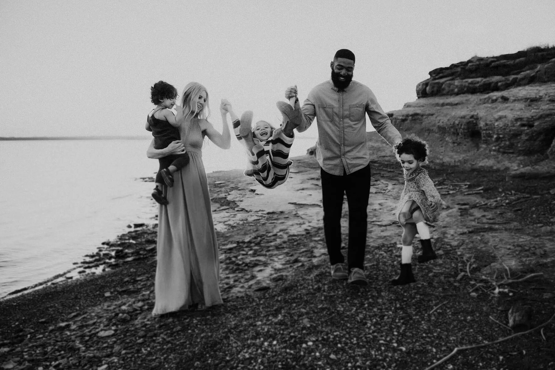 Black and white frame of a family swinging their child between them on the shoreline